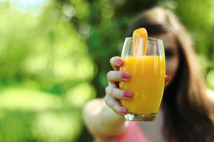 Dívka drží sklenici s pomerančovým džusem